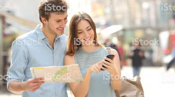istockphoto-475240290-2048×2048 Couple of tourists consulting a city guide and smartphone gps in the street searching locations